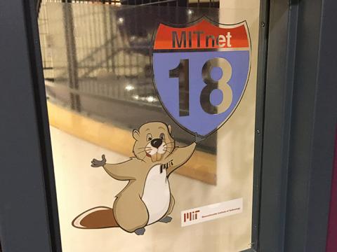 Sticker on a window of a beaver holding an MITnet 18 road sign.