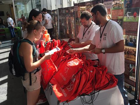 Picture of IS&T staff members handing out red MIT IST swag bags to MIT students.