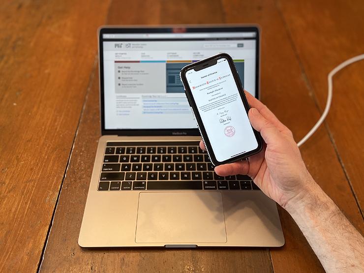 Hand holding a cellphone displaying a digital MIT diploma.
