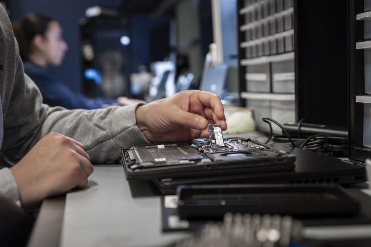 An employee holds a microchip as they fix a hardware device. 